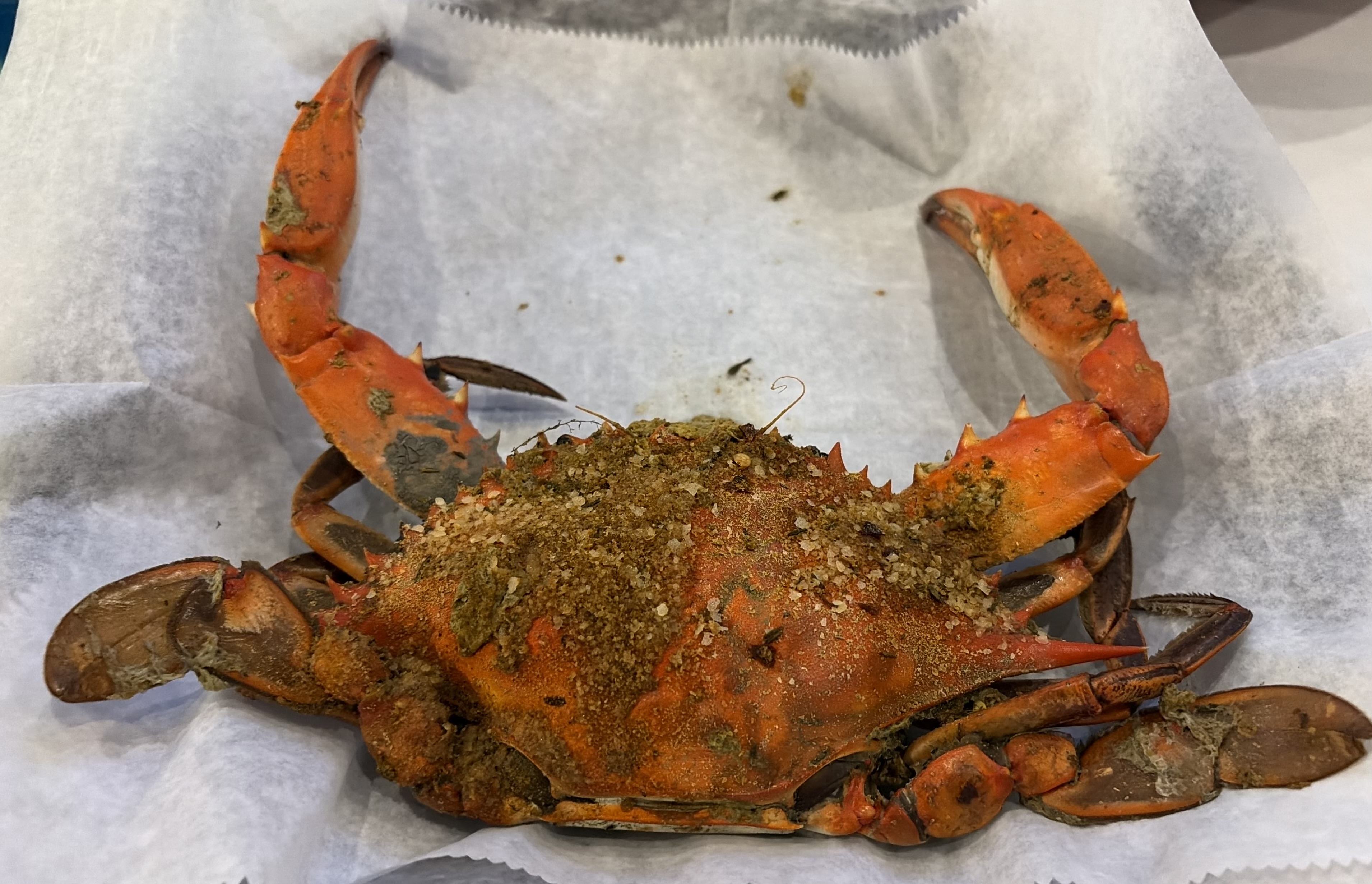 A whole blue crab buried in Old Bay-style seasoning and coarse salt on deli paper at Riggins Crabhouse